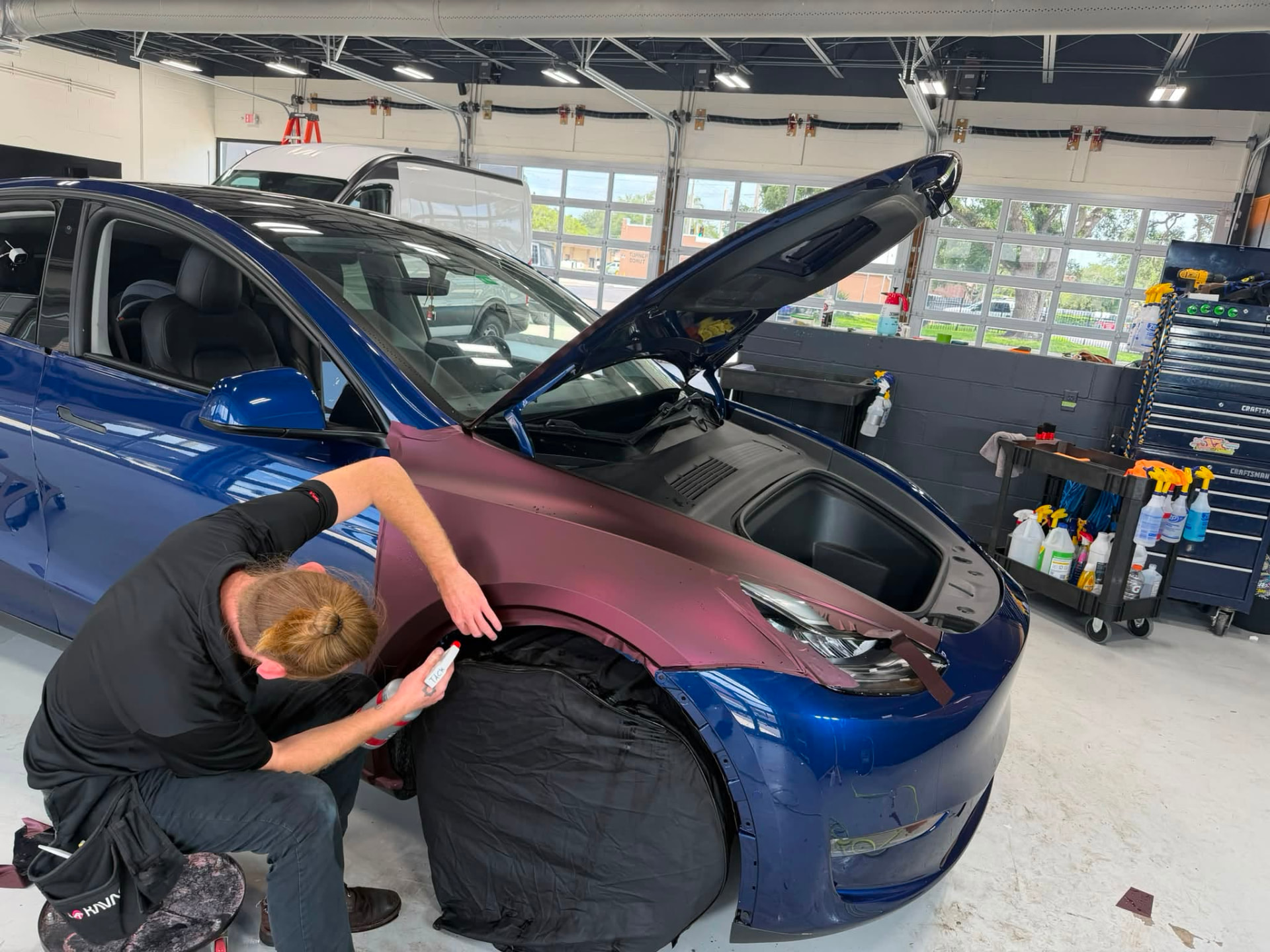 Technician laying vinyl wrap film across the front bodywork of a vehicle