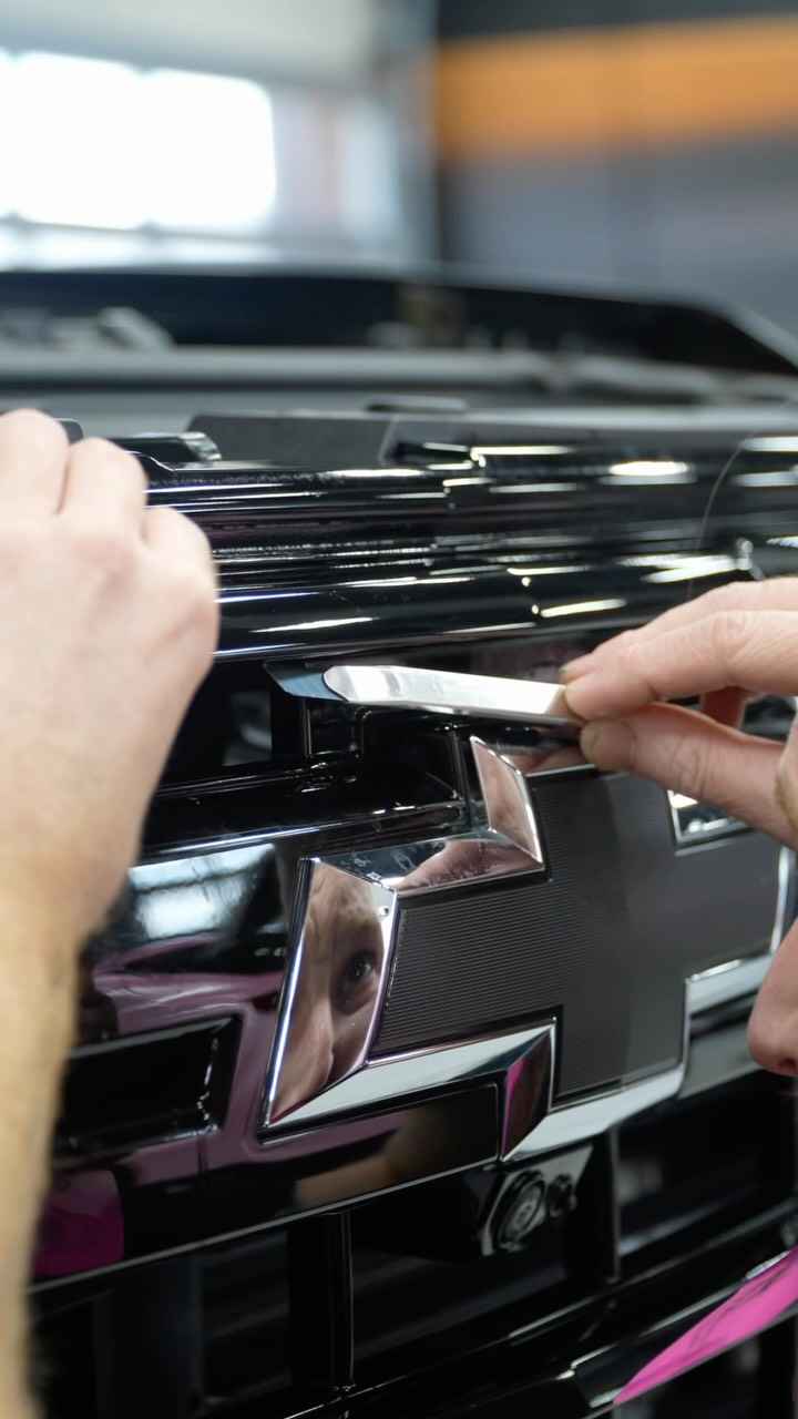 Installer tucking paint protection film into a black Chevrolet grille
